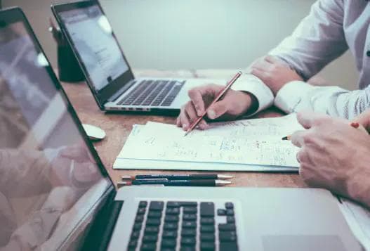 A closeup of laptops and a set of papers being discussed by two individuals